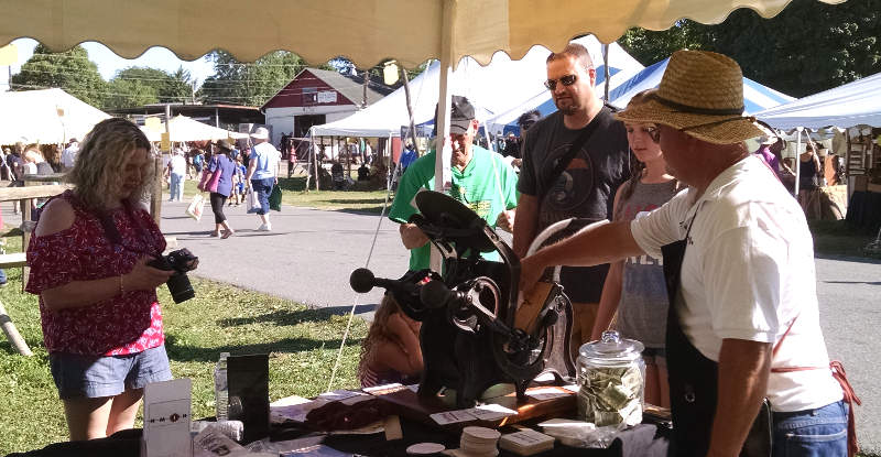 Frank. helping one of our younger visitors to the
                  NMIH tent at the Kutztown Folk Art Festival print her
                  own coaster on the Daughaday press